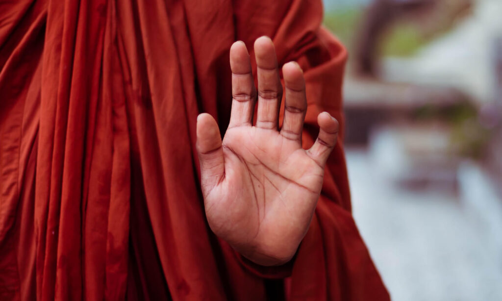 Ein buddhistischer Mönch hebt die Hand, sodass man seine Handfläche sehen kann.