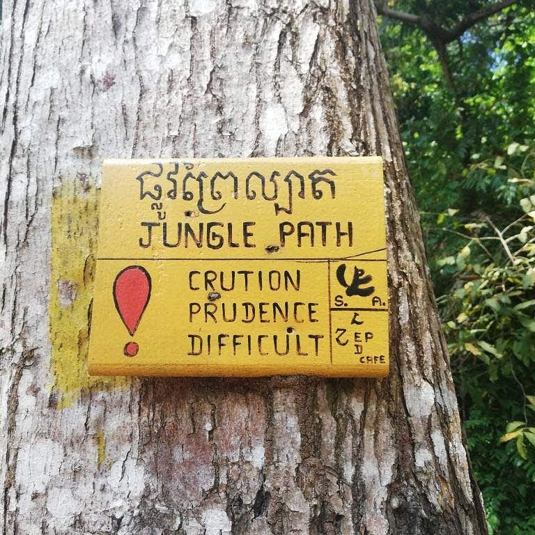 Ein gelbes Hinweisschild mit einer Warnung vor einem schwierigen Dschungel-Pfad im Nationalpark Kep, Kambodscha.