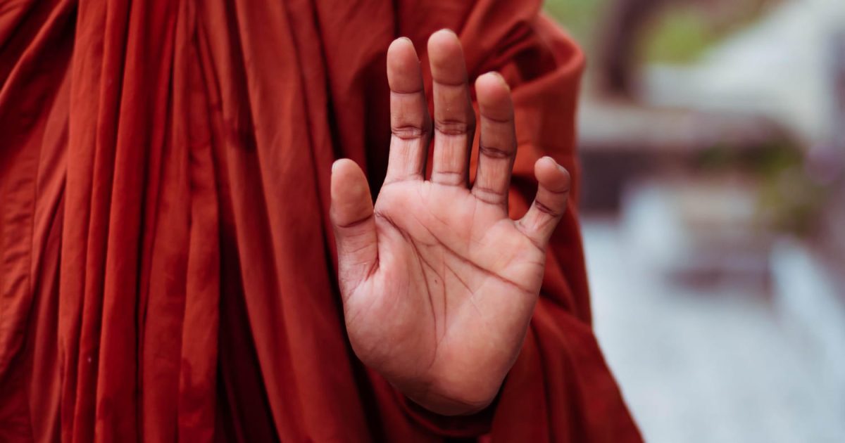 Ein buddhistischer Mönch hebt die Hand, sodass man seine Handfläche sehen kann.